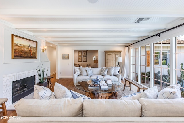 living room featuring visible vents, beamed ceiling, a brick fireplace, and wood finished floors