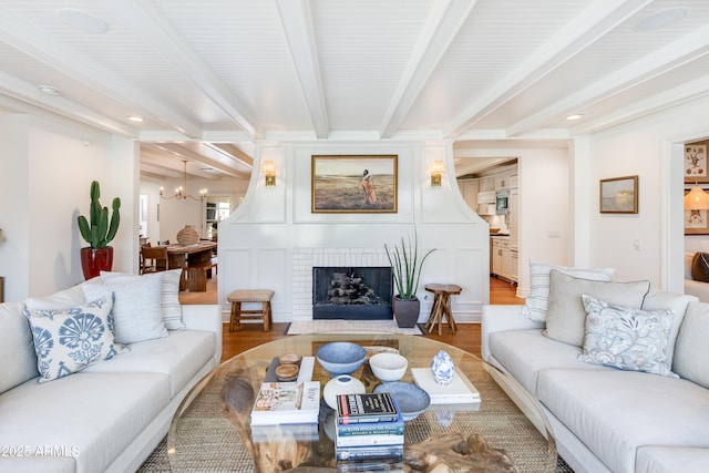 living area featuring beam ceiling, a notable chandelier, wood finished floors, a fireplace, and crown molding