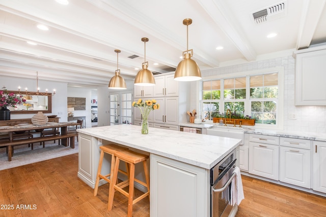 kitchen featuring beam ceiling, visible vents, light wood finished floors, and a center island