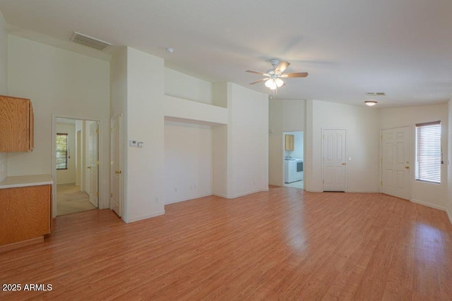 unfurnished living room with washer / clothes dryer, ceiling fan, and light hardwood / wood-style floors