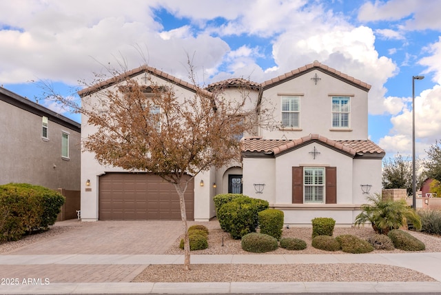 mediterranean / spanish house with stucco siding, an attached garage, a tile roof, and decorative driveway