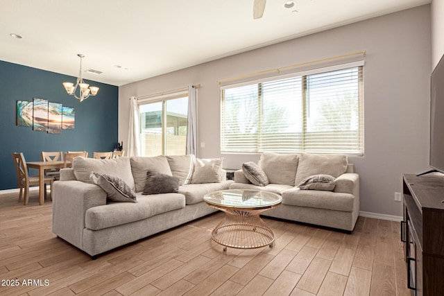 living room featuring light wood-style flooring, baseboards, and ceiling fan with notable chandelier