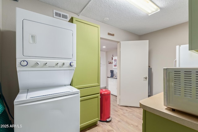 laundry area with stacked washer / drying machine, light hardwood / wood-style floors, and a textured ceiling