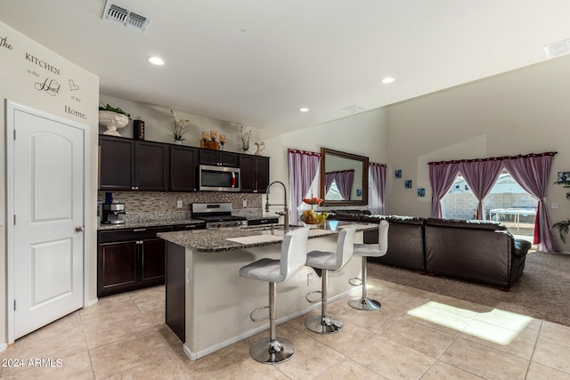 kitchen with appliances with stainless steel finishes, sink, a kitchen bar, dark stone countertops, and a center island with sink