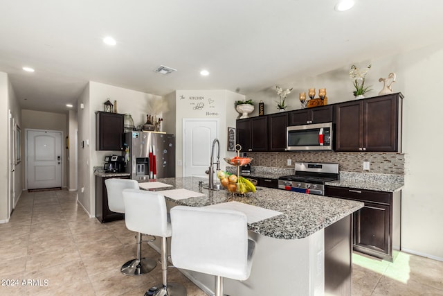 kitchen featuring decorative backsplash, appliances with stainless steel finishes, a kitchen bar, and a center island with sink