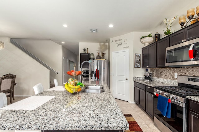 kitchen featuring a kitchen island with sink, stainless steel appliances, sink, light stone countertops, and light tile patterned floors