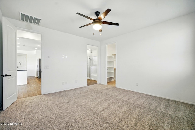 unfurnished bedroom with visible vents, baseboards, light colored carpet, a spacious closet, and ensuite bath