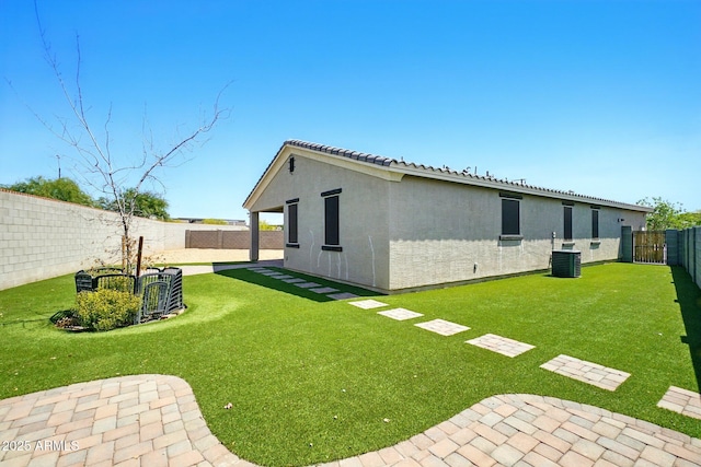 rear view of property with a fenced backyard, central AC unit, stucco siding, and a yard