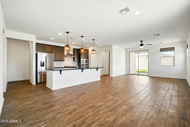 kitchen featuring dark countertops, open floor plan, a kitchen breakfast bar, recessed lighting, and appliances with stainless steel finishes