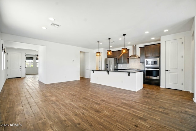 kitchen with a kitchen breakfast bar, visible vents, dark countertops, dark wood finished floors, and stainless steel appliances