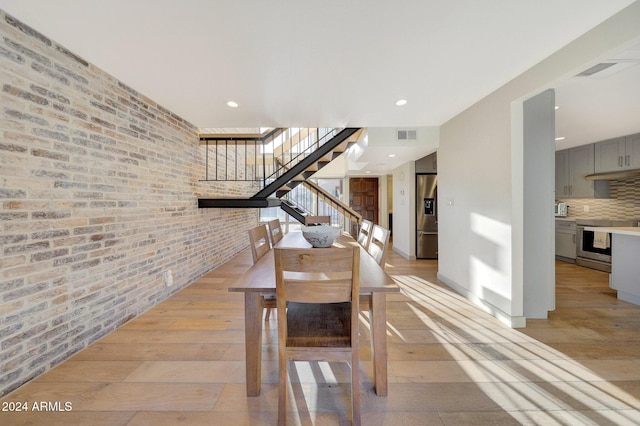 unfurnished dining area with light hardwood / wood-style flooring and brick wall