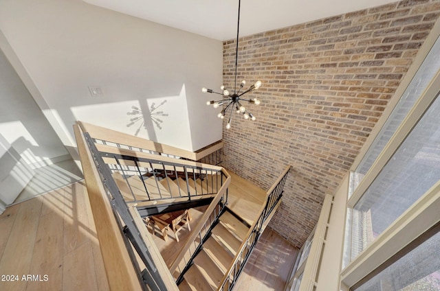 staircase featuring a towering ceiling, brick wall, a notable chandelier, and hardwood / wood-style flooring