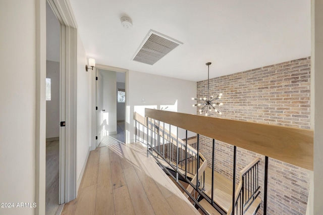 hall with a chandelier, light wood-type flooring, and brick wall