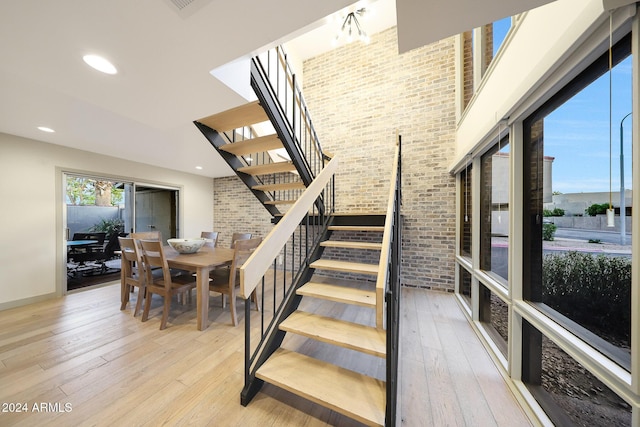 stairs with hardwood / wood-style floors, an inviting chandelier, and brick wall