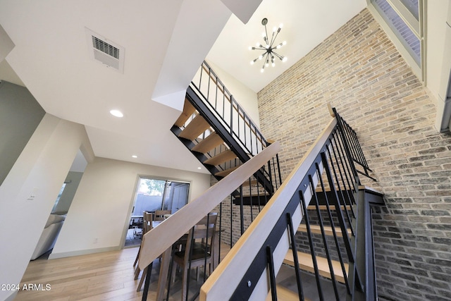 staircase featuring hardwood / wood-style floors, a high ceiling, a notable chandelier, and brick wall