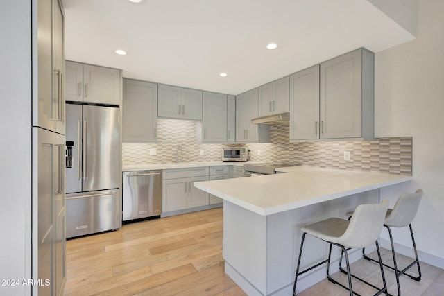 kitchen with kitchen peninsula, a kitchen bar, stainless steel appliances, and light hardwood / wood-style floors