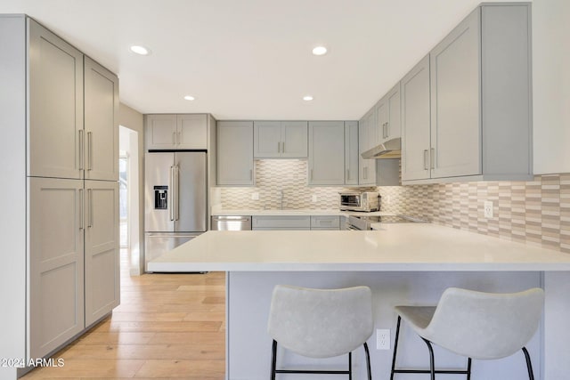 kitchen with a breakfast bar area, gray cabinets, light hardwood / wood-style floors, kitchen peninsula, and stainless steel appliances