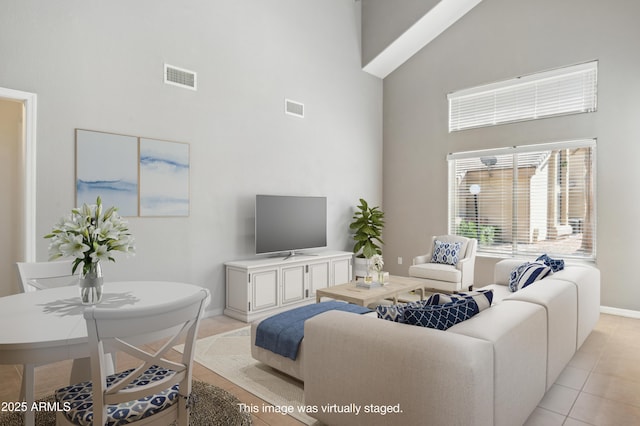 living area featuring a towering ceiling, light tile patterned floors, baseboards, and visible vents