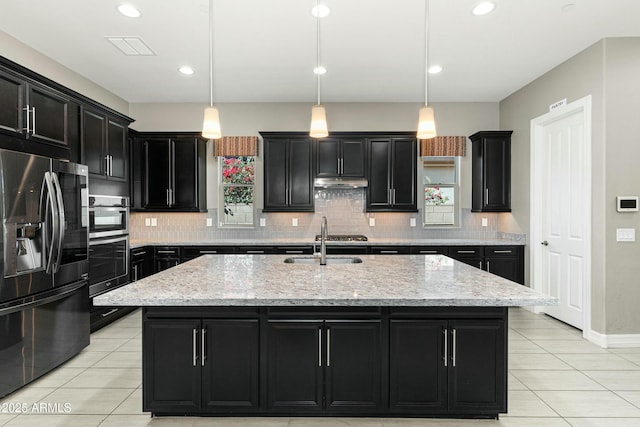 kitchen with hanging light fixtures, sink, a center island with sink, and stainless steel fridge