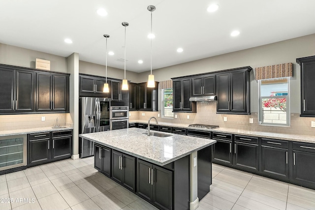 kitchen with pendant lighting, sink, appliances with stainless steel finishes, a kitchen island with sink, and light stone counters