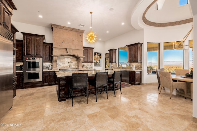 kitchen with a notable chandelier, a center island with sink, dark brown cabinets, light stone counters, and stainless steel appliances