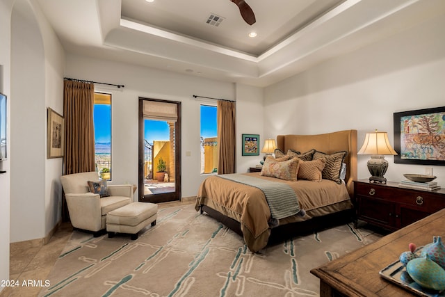 bedroom with multiple windows, access to outside, ceiling fan, and a tray ceiling