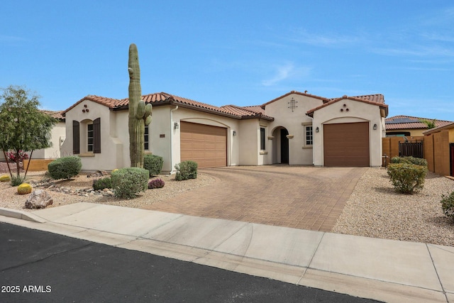 mediterranean / spanish-style house with a tile roof, decorative driveway, stucco siding, and an attached garage