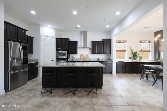 kitchen featuring stainless steel appliances, a breakfast bar, visible vents, wall chimney range hood, and a kitchen island with sink