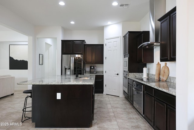kitchen featuring visible vents, a breakfast bar, stainless steel appliances, a sink, and wall chimney range hood