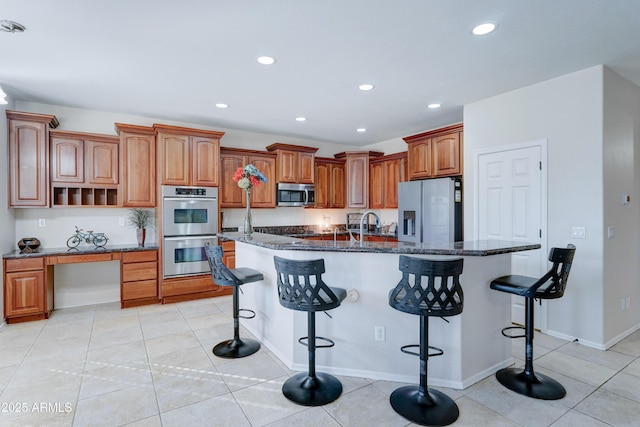 kitchen with dark stone counters, a center island with sink, stainless steel appliances, and a breakfast bar area