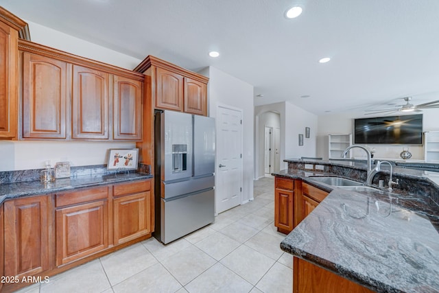 kitchen with ceiling fan, dark stone countertops, sink, stainless steel fridge with ice dispenser, and light tile patterned floors