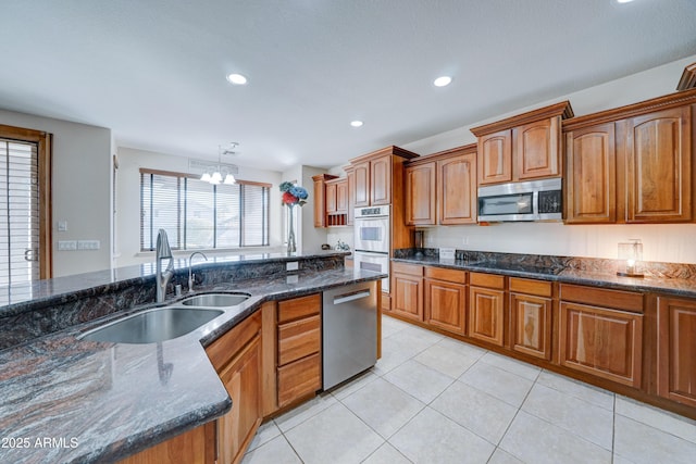 kitchen featuring pendant lighting, appliances with stainless steel finishes, dark stone counters, an inviting chandelier, and sink