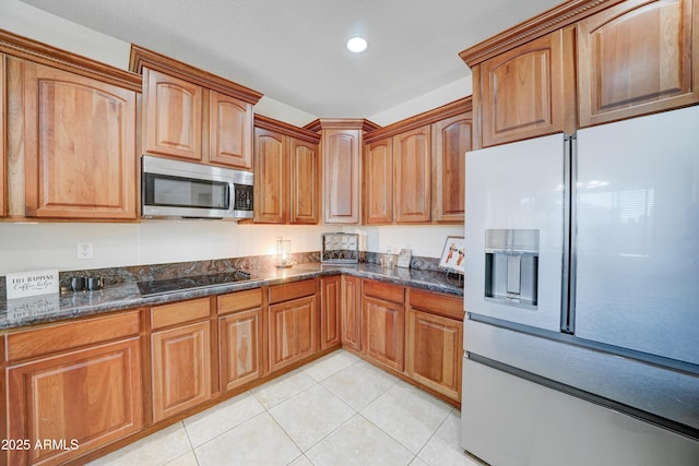 kitchen with light tile patterned floors, white refrigerator with ice dispenser, black electric cooktop, and dark stone counters