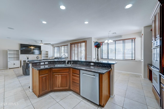 kitchen featuring stainless steel dishwasher, a kitchen island with sink, pendant lighting, ceiling fan with notable chandelier, and sink