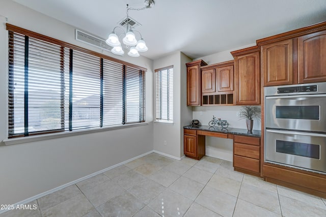 kitchen featuring light tile patterned flooring, dark stone countertops, double oven, and an inviting chandelier