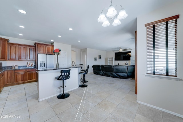 kitchen with light tile patterned floors, stainless steel refrigerator with ice dispenser, a breakfast bar area, pendant lighting, and ceiling fan with notable chandelier