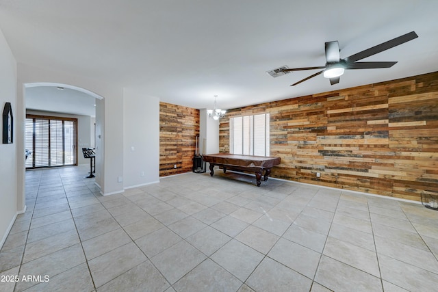 empty room featuring light tile patterned floors, ceiling fan with notable chandelier, pool table, and wood walls