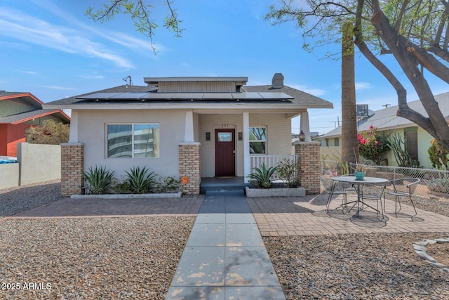 view of front facade featuring fence, covered porch, brick siding, solar panels, and a patio area