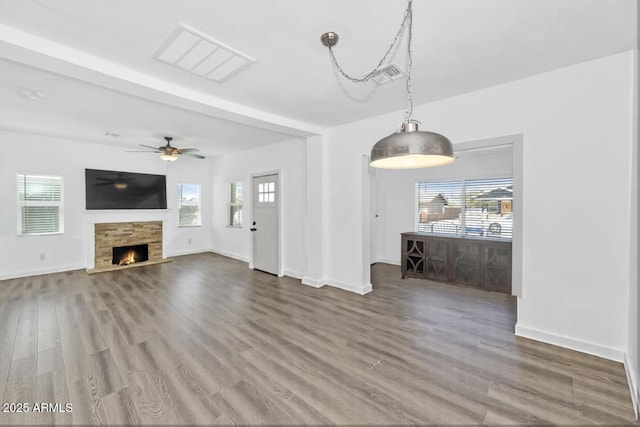 unfurnished living room with a stone fireplace, wood finished floors, and plenty of natural light