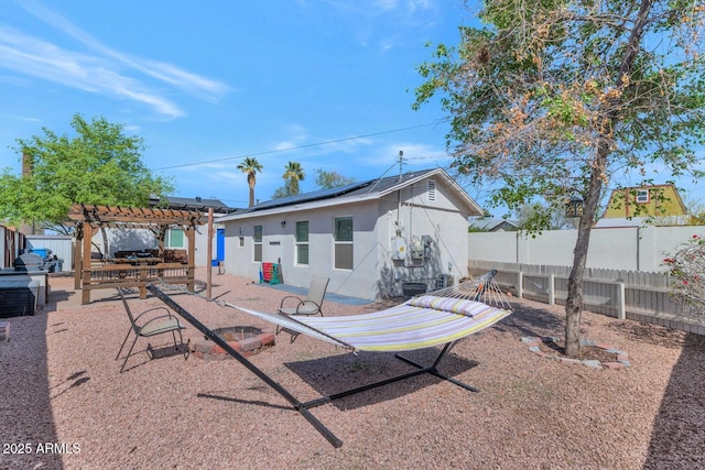 rear view of house with roof mounted solar panels, a patio, a fenced backyard, stucco siding, and a pergola