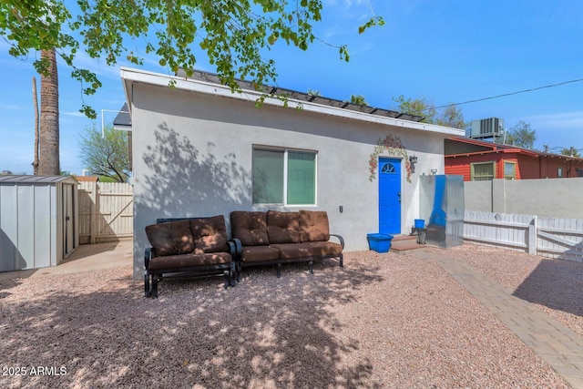 view of front of property featuring fence, stucco siding, cooling unit, an outdoor structure, and a shed