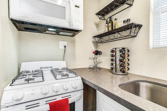 kitchen with white cabinetry, a textured wall, stone counters, and white appliances