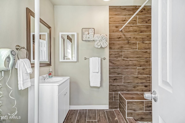 full bath with vanity, baseboards, a tile shower, and wood finished floors