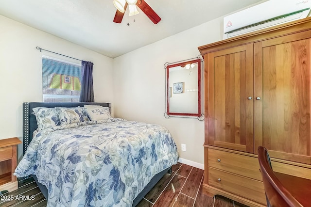 bedroom with wood finish floors, a wall unit AC, baseboards, and ceiling fan