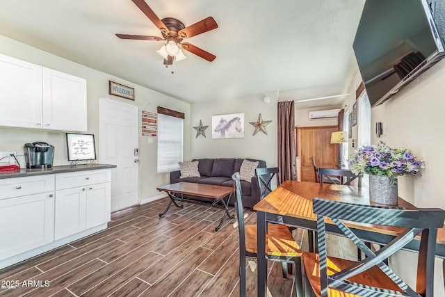dining room featuring baseboards, an AC wall unit, ceiling fan, and wood finish floors