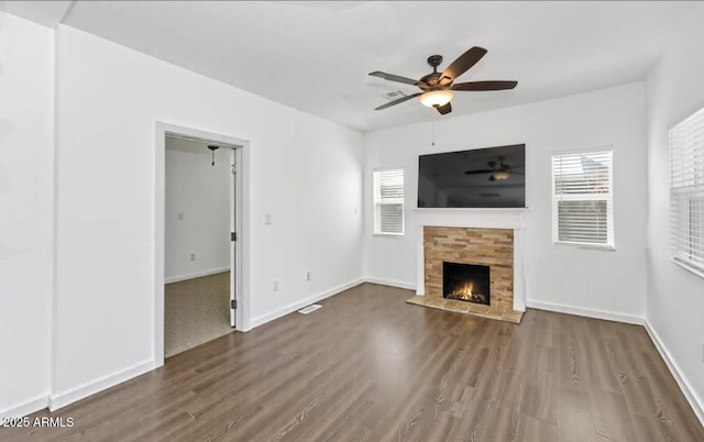 unfurnished living room featuring a stone fireplace, baseboards, ceiling fan, and wood finished floors