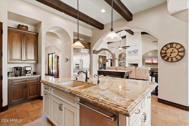 kitchen featuring a kitchen island with sink, beam ceiling, hanging light fixtures, appliances with stainless steel finishes, and light stone counters