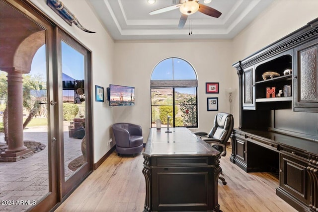 home office featuring french doors, a raised ceiling, ornate columns, ceiling fan, and light hardwood / wood-style flooring