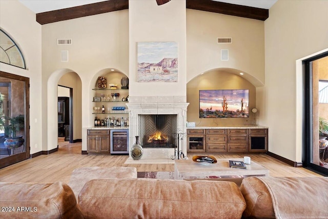 living room with wine cooler, high vaulted ceiling, built in features, and light hardwood / wood-style flooring