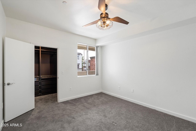 unfurnished bedroom featuring a closet, carpet, baseboards, ceiling fan, and a walk in closet